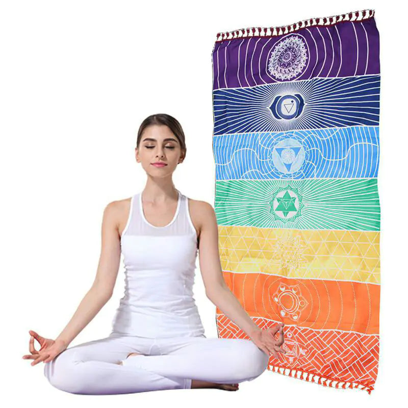 Woman in white outfit meditating next to a colorful towel with chakra designs. From ghg wellness shop.